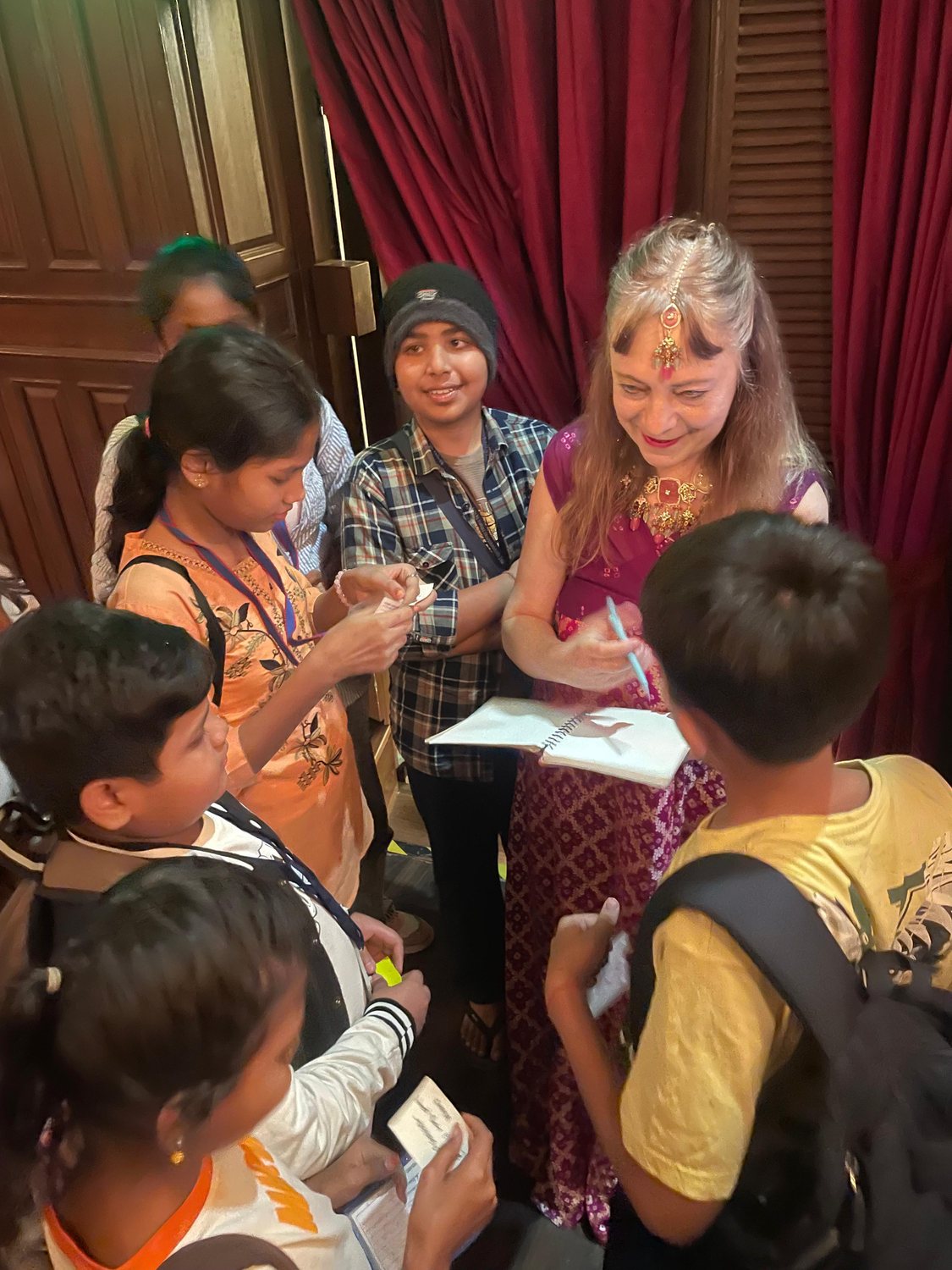 Katya signing autographs for a group of children in front of a red stage curtain