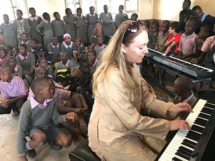 Katya playing a keyboard surrounded by schoolchildren sitting on the floor