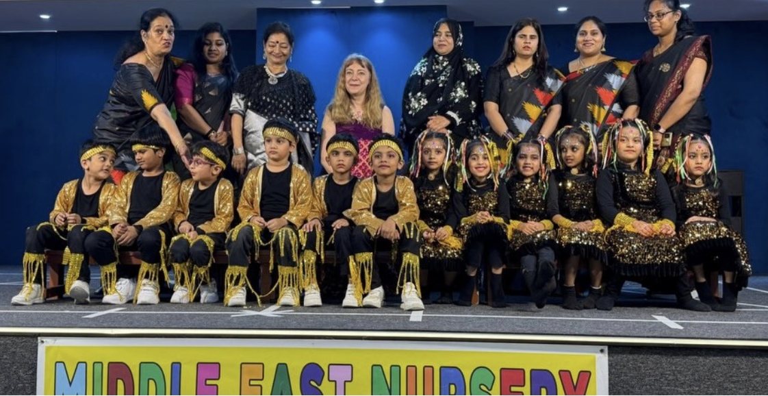 A stage group photo of children in costume standing with adults after a performance