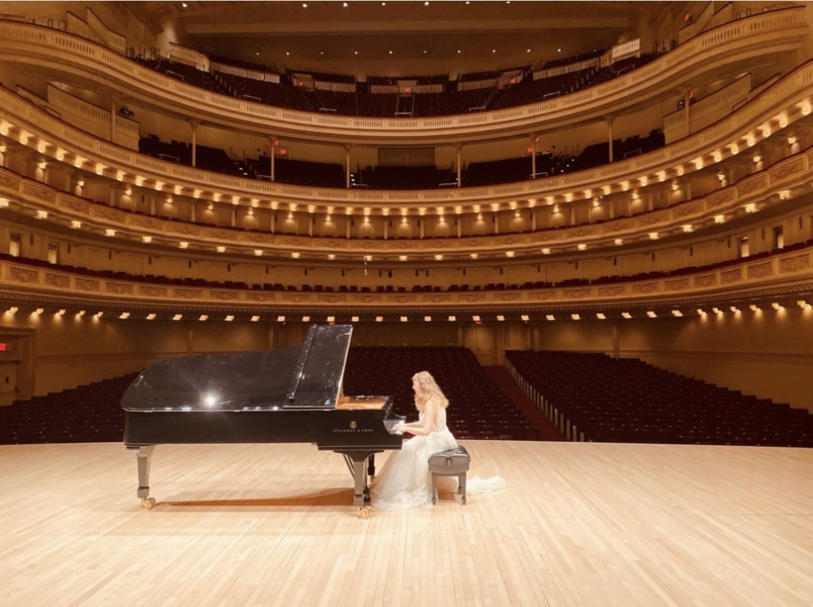 Katya Grineva sits alone at the grand piano on the Carnegie Hall stage, looking out over the vast, empty auditorium