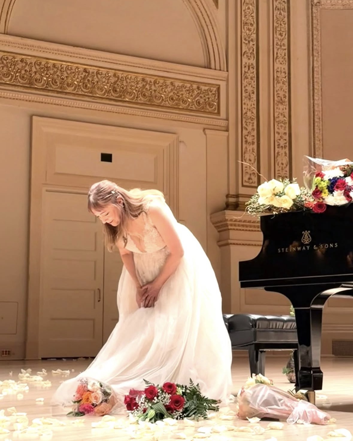 Katya Grineva takes a bow on the Carnegie Hall stage, surrounded by bouquets of flowers from the audience
